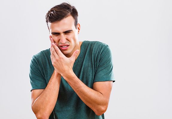 man in green t-shirt holding his mouth in pain 