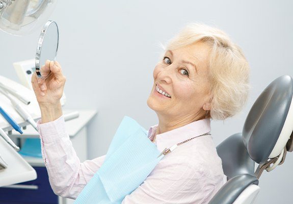 Woman looking at her new denture in hand mirror