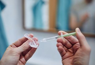 Someone applying bleaching gel to a teeth whitening tray