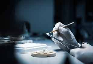 A closeup of a dental crown being processed by a lab worker