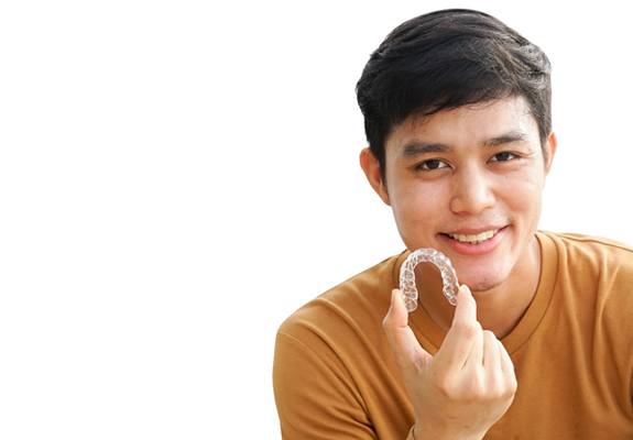 A young male teenager in an orange shirt and holding an Invisalign aligner