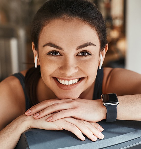 A smiling woman wearing headphones and a smart watch