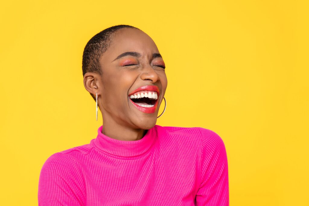 Woman in pink sweater smiling with eyes closed with yellow background